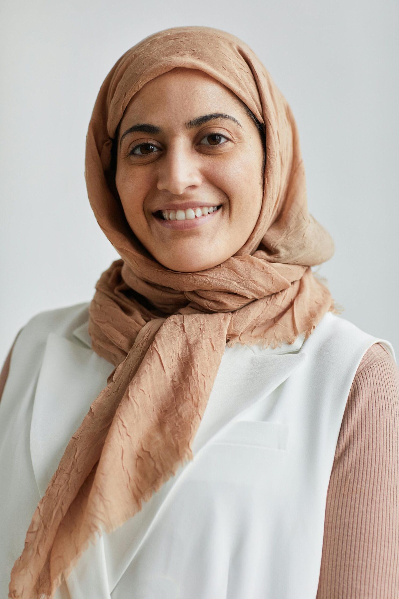 Portrait of a cheerful woman wearing a hijab and smiling against a white background.